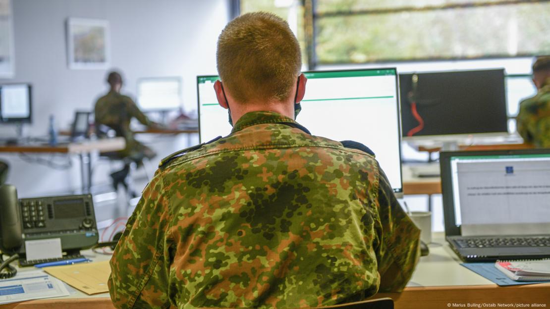 Foto interna mostra militares fardados em sala usando computadores