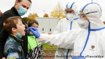 Немецкий медик в защитном костюме тестирует мальчика на коронавирус 