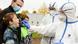 A child is tested with a swab by two medical professionals in protective gear A child is tested with a swab by two medical professionals in protective gear