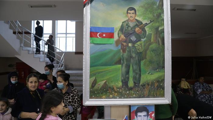 Perempuan dan anak-anak berada di ruangan dengan gambar seorang tentara yang meninggal
