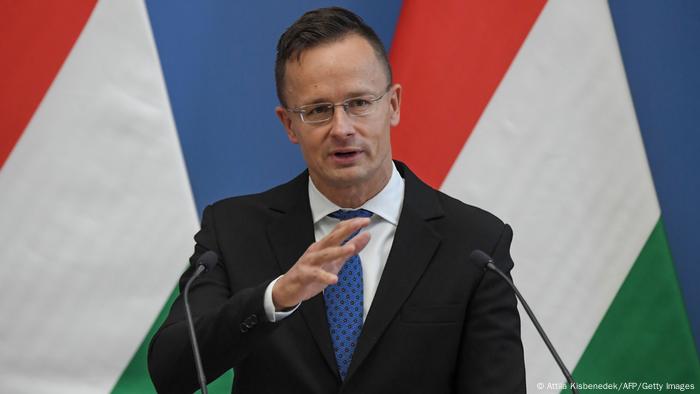 Peter Szijjarto, man speaking in front of two microphones, flag in the background 