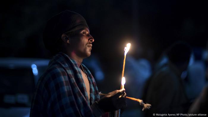 A man holds a candle in the dark during a church service A man holds a candle in the dark during a church service