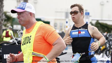 Chris Nikic (derecha) mientras corre junto a su acomompañante guía en el triatlón.