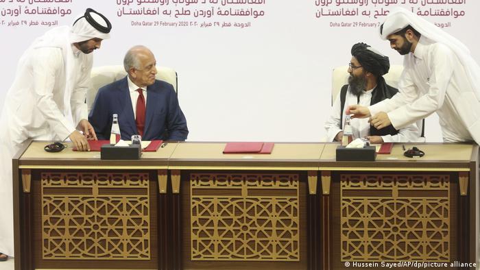 Der US-Sondergesandte Zalmay Khalilzad und der Taliban Mullah Abdul Ghani Baradar unterzeichnen an einem Tisch sitzend das Doha-Abkommen für Afghanistan.