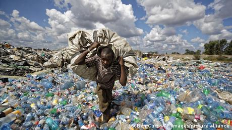 Un homme porte un sac en marchant à travers une montagne de bouteilles plastiques à Dandora au Kenya