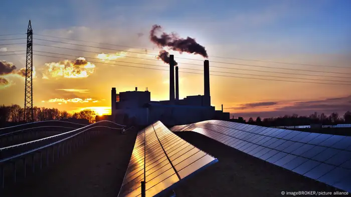 Solarpark und dahinter eine Fabrik im Sonnenlicht