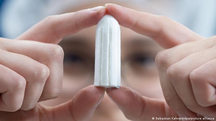 A woman in lab attire holding up a fat, unused tampon