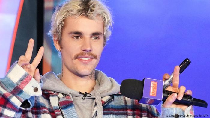 Justin Bieber sosteniendo el micrófono en una mano y haciendo el signo de la paz