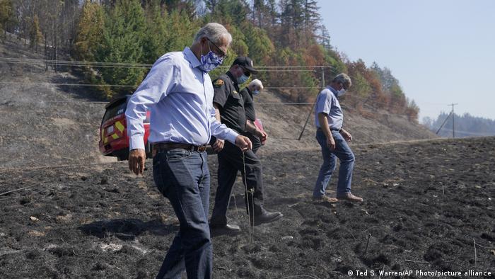 Washington Governor Jay Inslee walks through a fire-damaged landscape with a team of officials