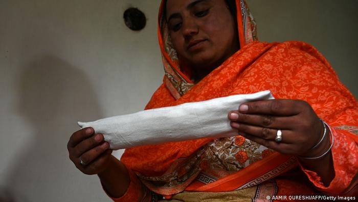 A Pakistani woman holds a sanitary pad she is making with a sewing machine
