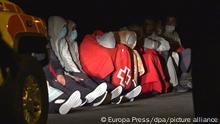 24.11.2020, Spanien, Lanzarote: Migranten sitzen umhüllt in Decken des Roten Kreuzes auf dem Boden. Beim Untergang ihres Holzbootes aus Nordafrika sind an der Küste der zu Spanien gehörenden Kanareninsel Lanzarote mindestens sieben Menschen ertrunken. Foto: Europa Press/EUROPA PRESS/dpa +++ dpa-Bildfunk +++ |