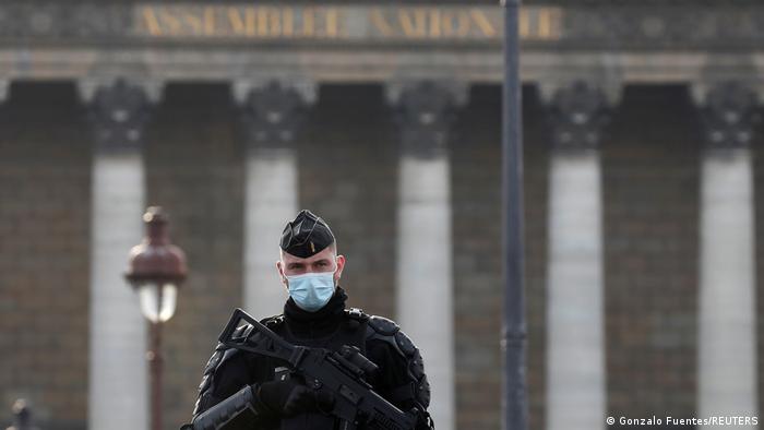 Policial de máscara protetora diante do prédio da Assembleia Nacional da França
