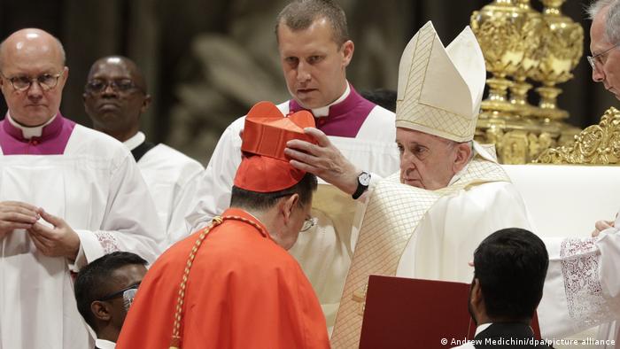 Francisco, de blanco, coloca un sombrero rojo en la cabeza de un nuevo cardenal entre otros clérigos