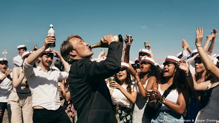 Szene aus Der Rausch - Mann trinkt aus Flasche, umringt von Menschen