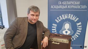 Andrej Bastunez sitzt vor dem Logo des Belarussischen Journalistenverbands