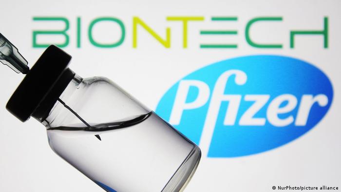 An ampoule with a vaccine against the background of the logos of Bayontek and Pfizer