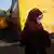 Mulher de véu e máscara protetora diante de ônibus amarelos
