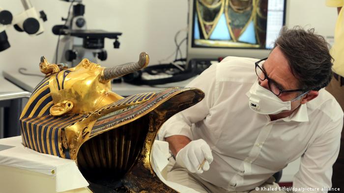 Konservator Christian Eckmann beugt sich mit Mundschutz und Pinzette über die goldene Maske von Tutanchamun 