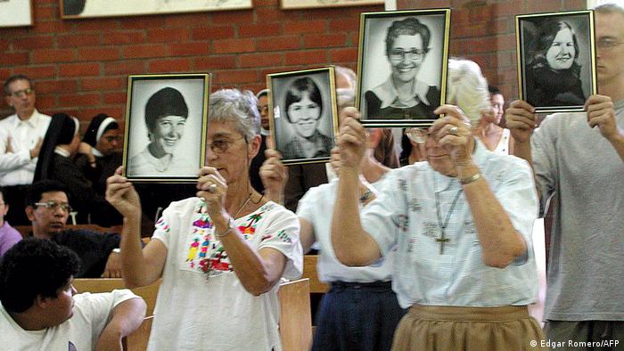 Foto de personas que sostienen fotos de las cuatro misioneras asesinadas en El Salvador.