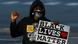 Person with a hoodie and a face mask makes a fist and holds a sign that reads Black Lives Matter Person with a hoodie and a face mask makes a fist and holds a sign that reads Black Lives Matter