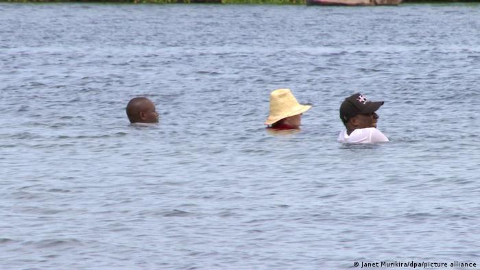 Three heads visible in a body of water, with a woman wearing a yellow hat and a man wearing a baseball cap. 