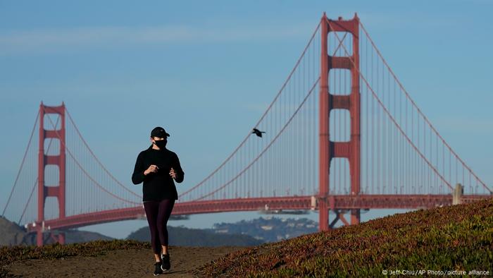 Woman wearing face mask jogs in front of Golden Gate Bridge background