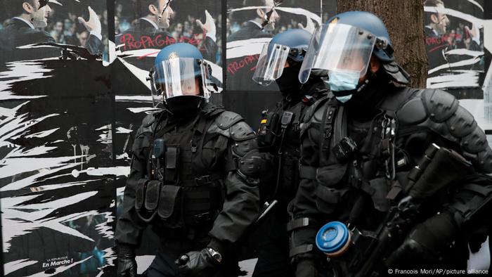 Riot police officers walk past defaced posters for French President Emmanuel Macron during a demonstration in Paris