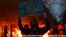 A protester holds a sign reading Sweet France. Dear country of violence in front of a fire during a demonstration for 'social rights' and against the 'global security' draft law, which Article 24 would criminalise the publication of images of on-duty police officers with the intent of harming their 'physical or psychological integrity', in Paris, on December 5, 2020. (Photo by Anne-Christine POUJOULAT / AFP) (Photo by ANNE-CHRISTINE POUJOULAT/AFP via Getty Images)