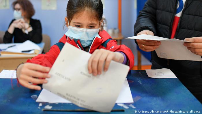 O fetiță cu mască introduce un buletin de vot în urnă la scrutinul din 6 decembrie 