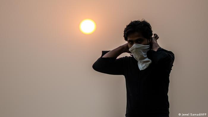 A man surrounded by smog wears a scarf around his face.