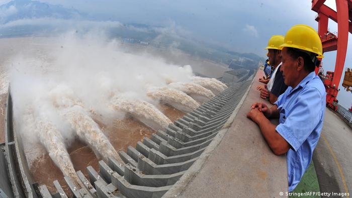Trabalhadores observam fluxo de água do alto de barragem