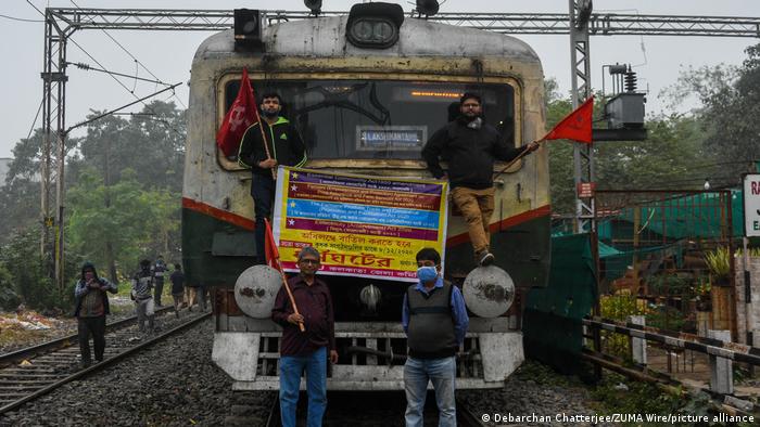 Four men stand in front of and on a stationary train holding a banner and flags