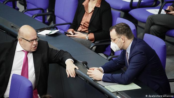 Auf seinem Stuhl im Bundestag dreht sich Wirtschaftsminister Peter Altmaier nach hinten um zu Gesundheitsminister Jens Spahn, der einen Mund-Nasen-Schutz trägt