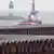 Gestapelte Rohre, im Hintergrund ein Leuchtturm und ein Schiff, das Richtung Meer fährt