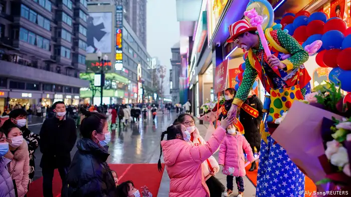Ein Kind reicht einem Clown in einer Einkaufsstraße die Hand