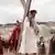 Film still The New Gospel, a man carrying a huge wooden cross accompanied by a Roman sodier