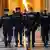 Policiais com uniformes e chapéus pretos, e com máscaras devido à pandemia de coronavírus, fazem a escolta em um tribunal de Paris. Eles estão de costas e caminham em um longo corredor.