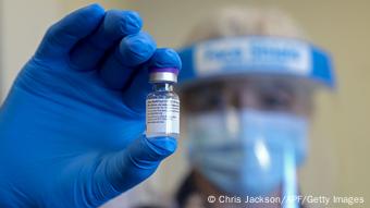 Медработник в Великобритании в перчатках и защитной маске показывает ампулу с вакциной от коронавируса производства BioNTech/Pfizer
