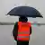 Ein Mann mit Regenschirm und orangener Weste mit der Aufschrift "Get ready for Brexit"