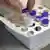 Zwei Finger ziehen eine Ampulle mit Corona-Impfstoff von BioNTech/Pfizer aus einem kleinen Karton