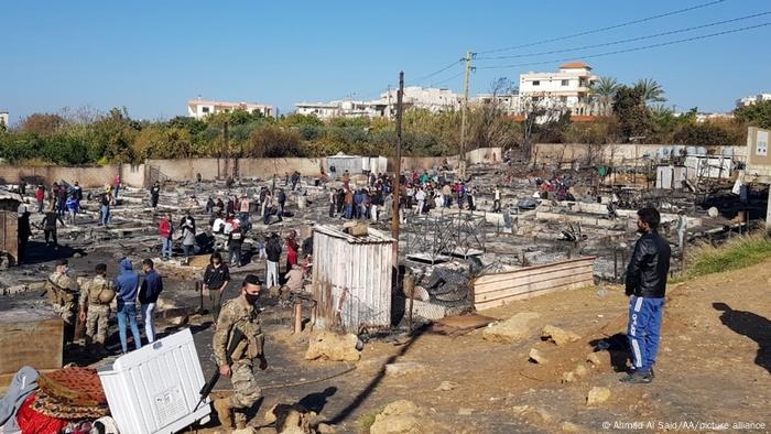 People mill around the remnants of a Syrian refugee camp after it was set on fire on fire during clashes with Lebanese locals