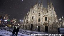 A picture taken on December 28, 2020 shows people walking on the snow-covered pavement past the Duomo's Cathedral in the center of Milan. (Photo by Miguel MEDINA / AFP) (Photo by MIGUEL MEDINA/AFP via Getty Images)