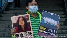 28.12.2020, China, Hongkong: Ein pro-demokratischer Aktivist zeigt zwei Plakate vor dem Verbindungsbüro der chinesischen Zentralregierung. Auf einem Plakat ist ein Foto der chinesischen Journalistin Zhang Zhan zu sehen. Zhang, eine ehemalige Anwältin und Journalistin aus Shanghai, wurde wegen ihrer Berichterstattung über den ersten Ausbruch des Coronavirus in Wuhan zu vier Jahren Gefängnis verurteilt. Die Aktivisten fordern die Freilassung von Zhang, sowie der 12 Hongkonger Aktivisten, die von den chinesischen Behörden auf See festgehalten werden. Foto: Kin Cheung/AP/dpa +++ dpa-Bildfunk +++