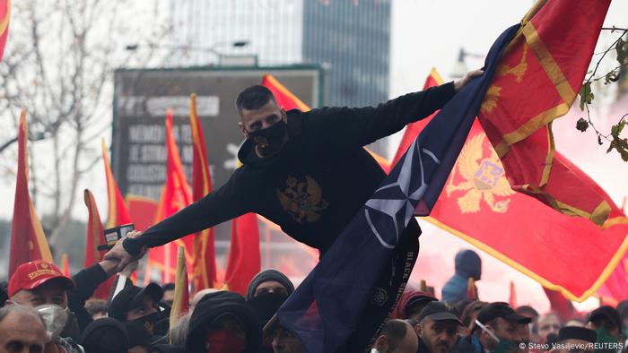 A Montenegro protester balances on the fence in front of the parliament while holding up flags of Montenegro and NATO