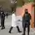 Ein Mann im weißen Kittel bringt unter Polizeischutz Impfdosen in ein Gebäude