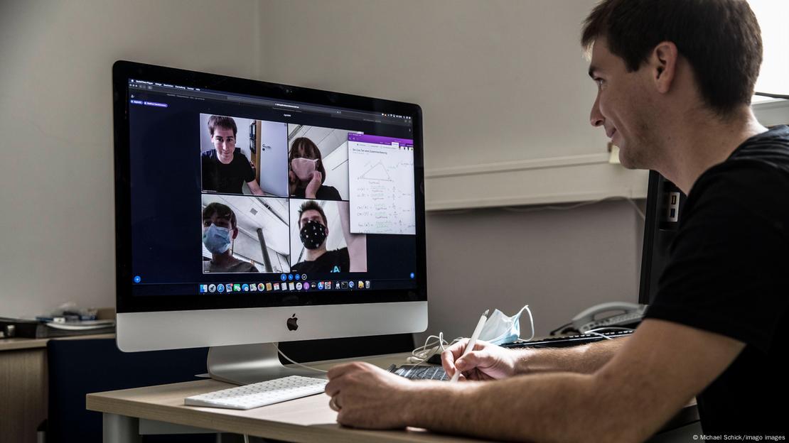 A student sitting at his computer taking part in an online class, with four other people on the computer screen