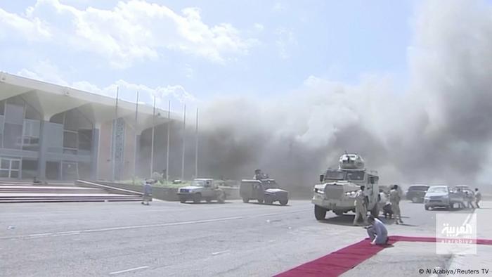 Dust from an explosion is strewn across an airport, in front of an airport building