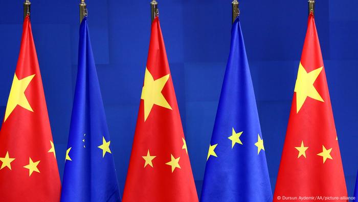 Drei Chinesische Flaggen und zwei europäische Sternenbanner im Wechsel nebeneinander vor blauer Wand