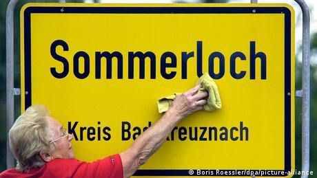 Eine Frau reinigt das Ortsschild „Sommerloch“