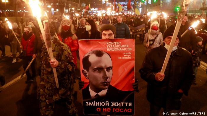 Crowd at night with torches, holding a poster with a picture of Stepan Bandera 
